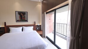 A hotel room with a large bed, a nightstand, a wall-mounted lamp, a painting, and a balcony with a view. - la mishika (Tarapith)