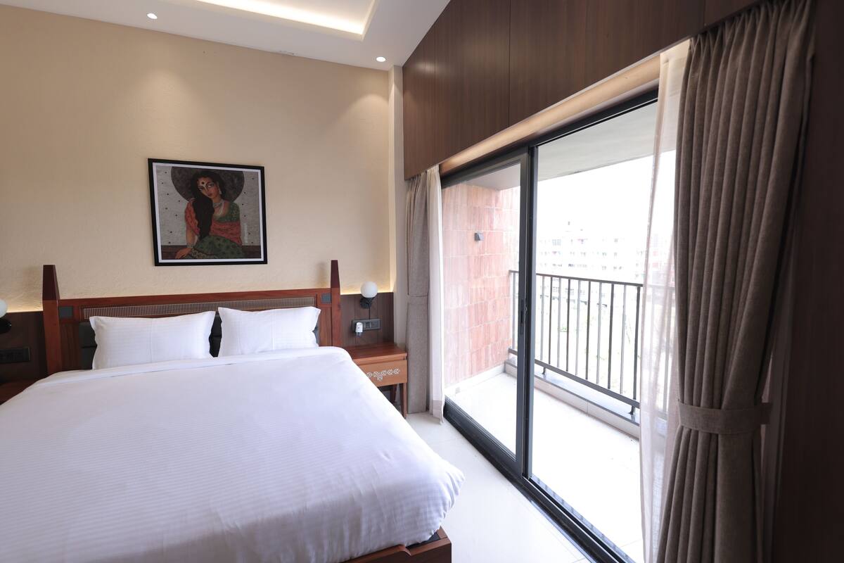 A hotel room with a large bed, a nightstand, a wall-mounted lamp, a painting, and a balcony with a view.