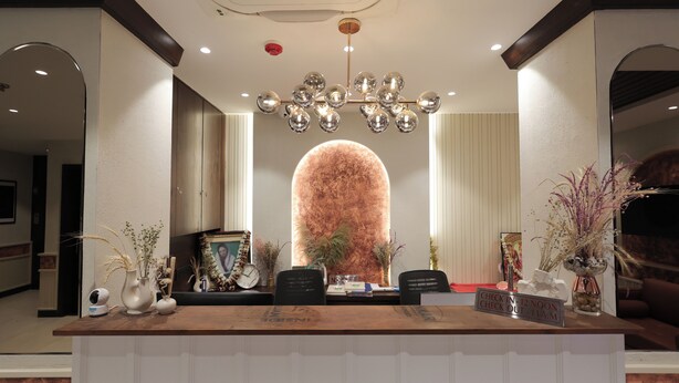 A reception desk with a sign indicating check-in times, a large decorative wall, and several potted plants. - la mishika (Tarapith)