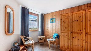 Een kamer met houten paneelwanden, een grote garderobe, twee rieten stoelen, een klein rond tafeltje en een bank.