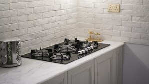 Una cocina con un salpicadero de ladrillo blanco, estufa a gas y un lavamanos pequeño.