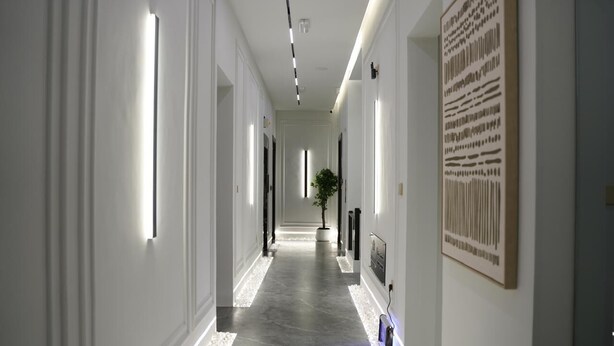Un pasillo moderno de hotel con un diseño largo y recto, iluminación empotrada, una planta en maceta y una obra de arte grande enmarcada en la pared.