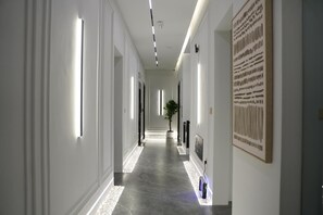Un pasillo moderno de hotel con un diseño largo y recto, iluminación empotrada, una planta en maceta y una obra de arte grande enmarcada en la pared.