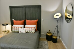 A bedroom with a bed, two nightstands, a floor lamp, a mirror, and a small table with decorative items. - Guestready - Casa das Arcadas (Ponta Delgada)