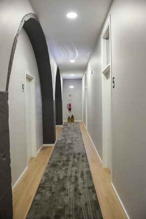 A hallway with white walls, wooden flooring, and a grey carpet. There are doors numbered 9 and 5, and a fire extinguisher mounted on the wall. - Guestready - Casa das Arcadas (Ponta Delgada)