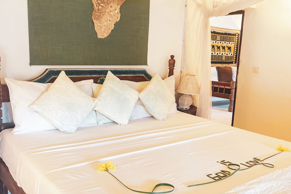 A neatly made bed with a decorative headboard, a large wall tapestry, and a canopy bed.