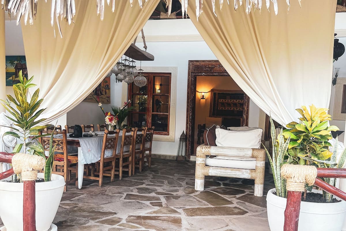 An outdoor seating area with a stone floor, a thatched roof, and potted plants.