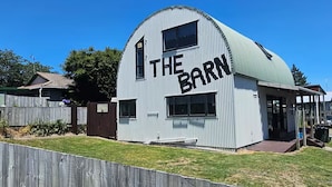 Ein weißes Getreidespeicher mit der Aufschrift "THE BARN" an der Seite, ein Holzzaun im Vordergrund und ein strahlend blauer Himmel im Hintergrund.