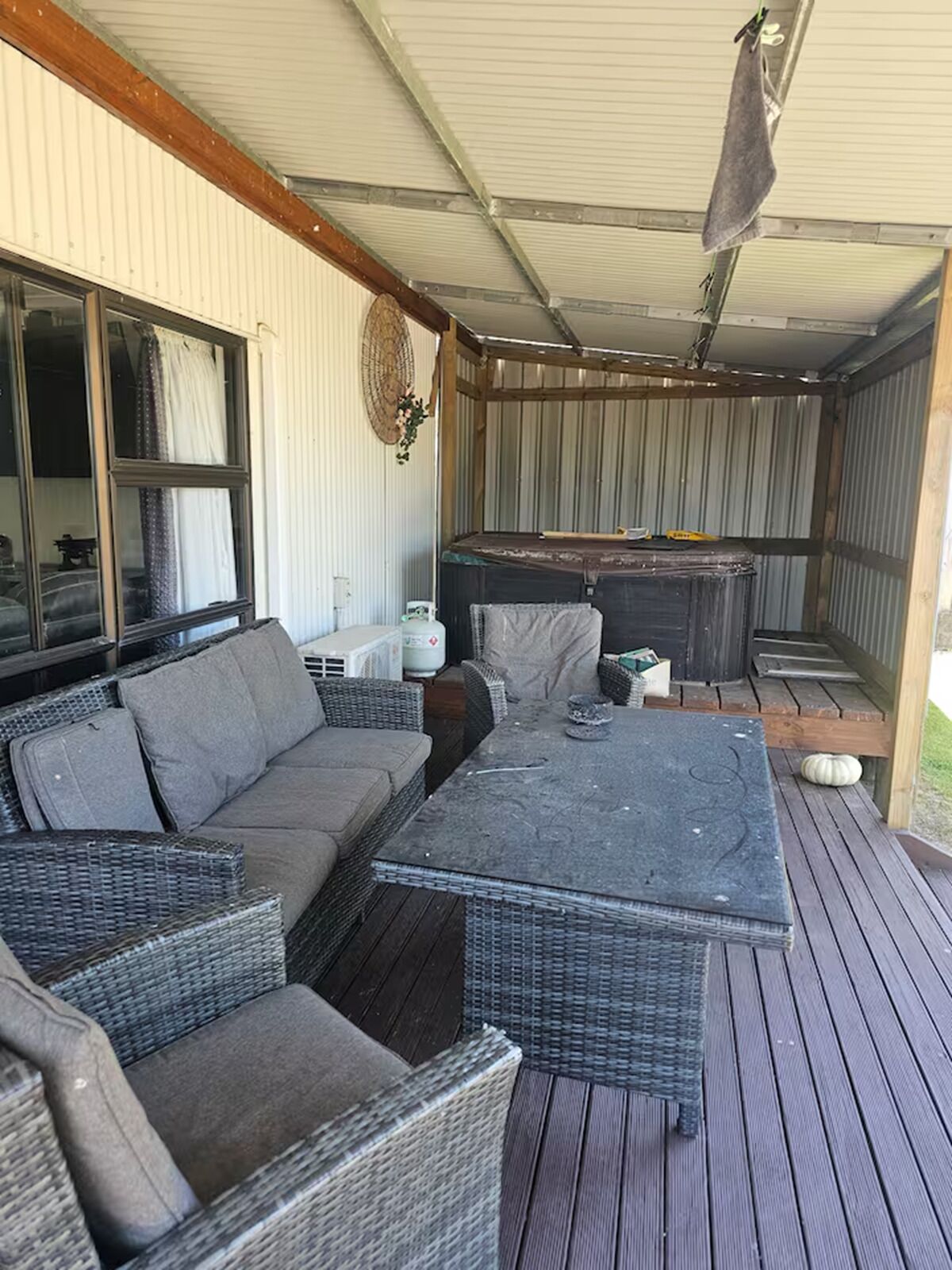 An outdoor covered patio with wicker furniture, a table, and a hot tub.