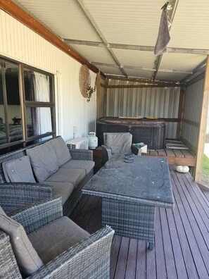 An outdoor covered patio with wicker furniture, a table, and a hot tub. - The Barn, 4 bedrms, Harry Potter rm, pet friendly (Rotorua)