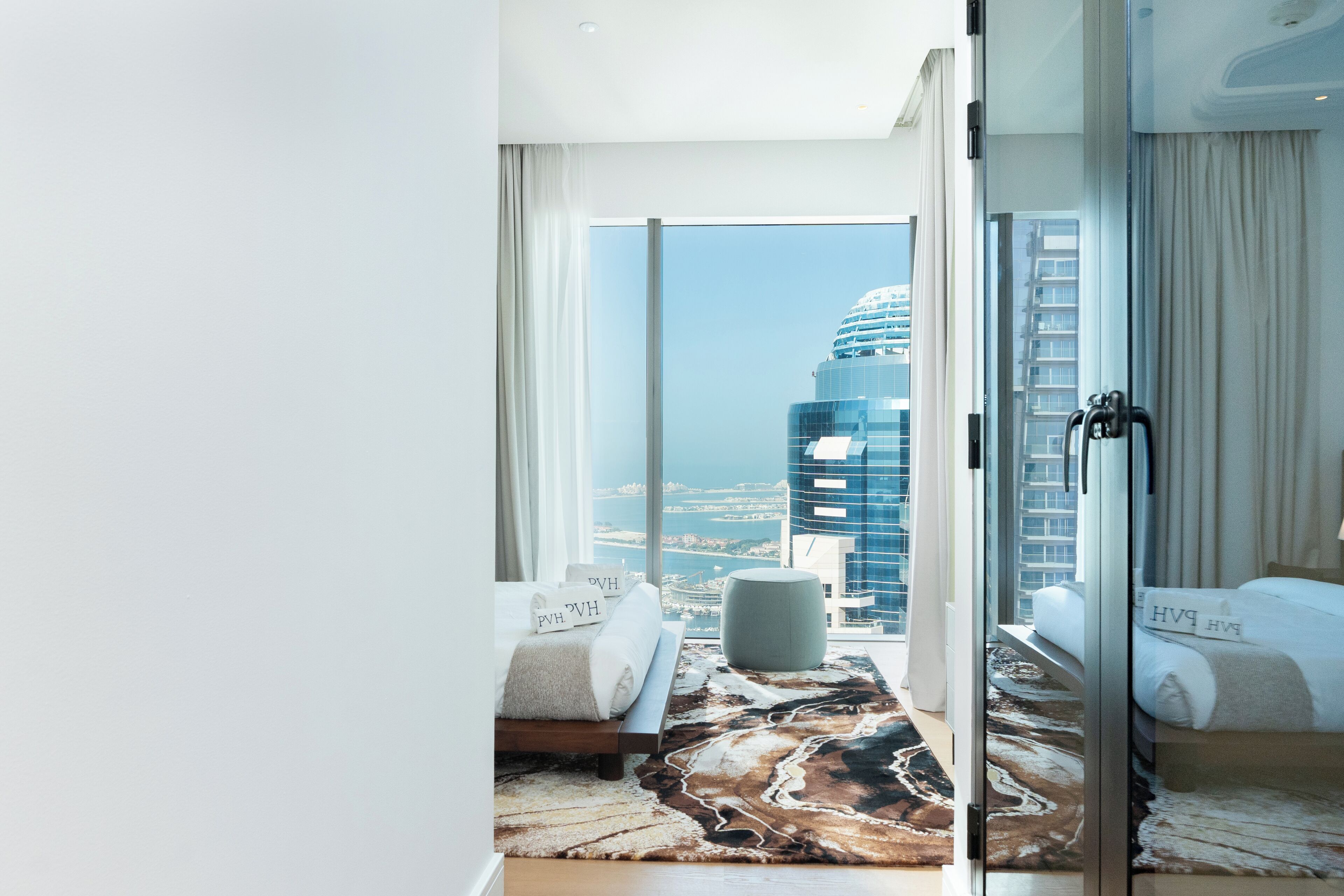 A modern hotel room with a large sliding glass door leading to a balcony, offering a city view.