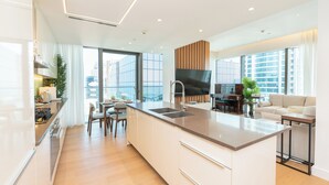 Una cocina moderna con una isla central, comedor con sillas, un sofá y un televisor.