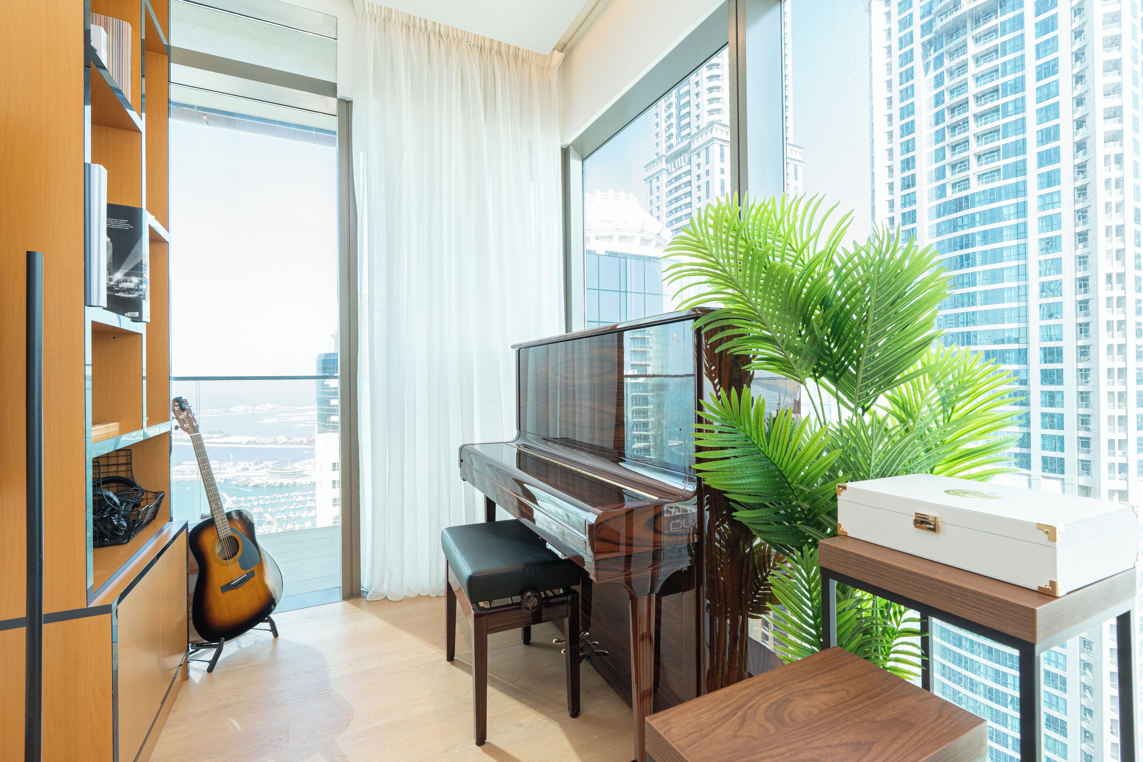 A modern living room with a grand piano, a guitar, a large potted plant, and a view of a cityscape through large windows.