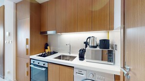 A modern kitchen with wooden cabinets, a stainless steel sink, a built-in oven, and a dishwasher. - Modern Studio l Community Views l Free Gym, Pool (Studio City)