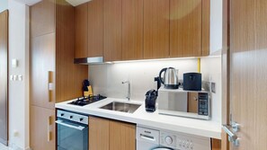 A modern kitchen with wooden cabinets, a stainless steel sink, a built-in oven, and a dishwasher. - Modern Studio l Community Views l Free Gym, Pool (Studio City)