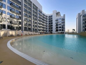 A modern hotel with a large pool, multiple balconies, and a clear sky. - Modern Studio l Community Views l Free Gym, Pool (Studio City)