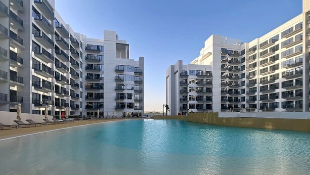 A modern hotel with a large pool, multiple balconies, and a clear sky. - Modern Studio l Community Views l Free Gym, Pool (Studio City)