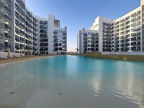 A modern hotel with a large pool, multiple balconies, and a clear sky. - Modern Studio l Community Views l Free Gym, Pool (Studio City)