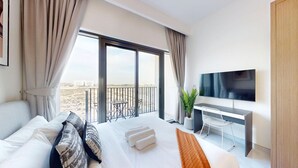 A modern hotel room with a large bed, a desk, a TV, and a balcony with a view of the beach. - Modern Studio l Community Views l Free Gym, Pool (Studio City)