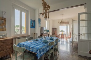 Un coin repas avec une nappe bleue à motifs, des chaises en bois et un lustre.