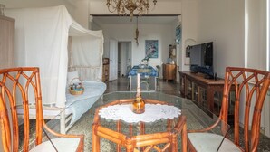 Una habitación con una cama cubierta de sábanas blancas, una mesa de comedor con sillas, un candelabro y un televisor.
