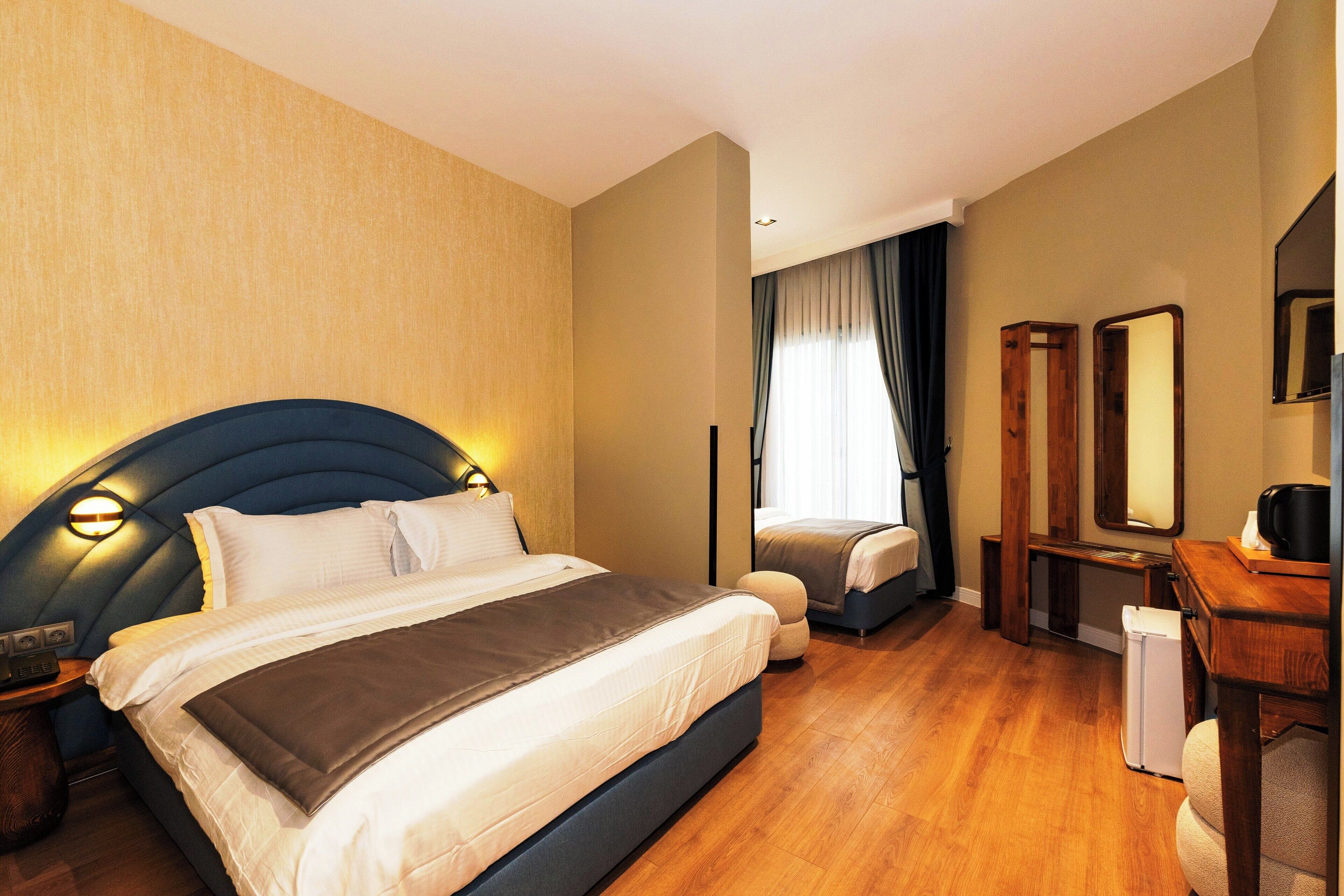 A hotel room with a large bed, a desk, a chair, a mirror, and a small refrigerator.