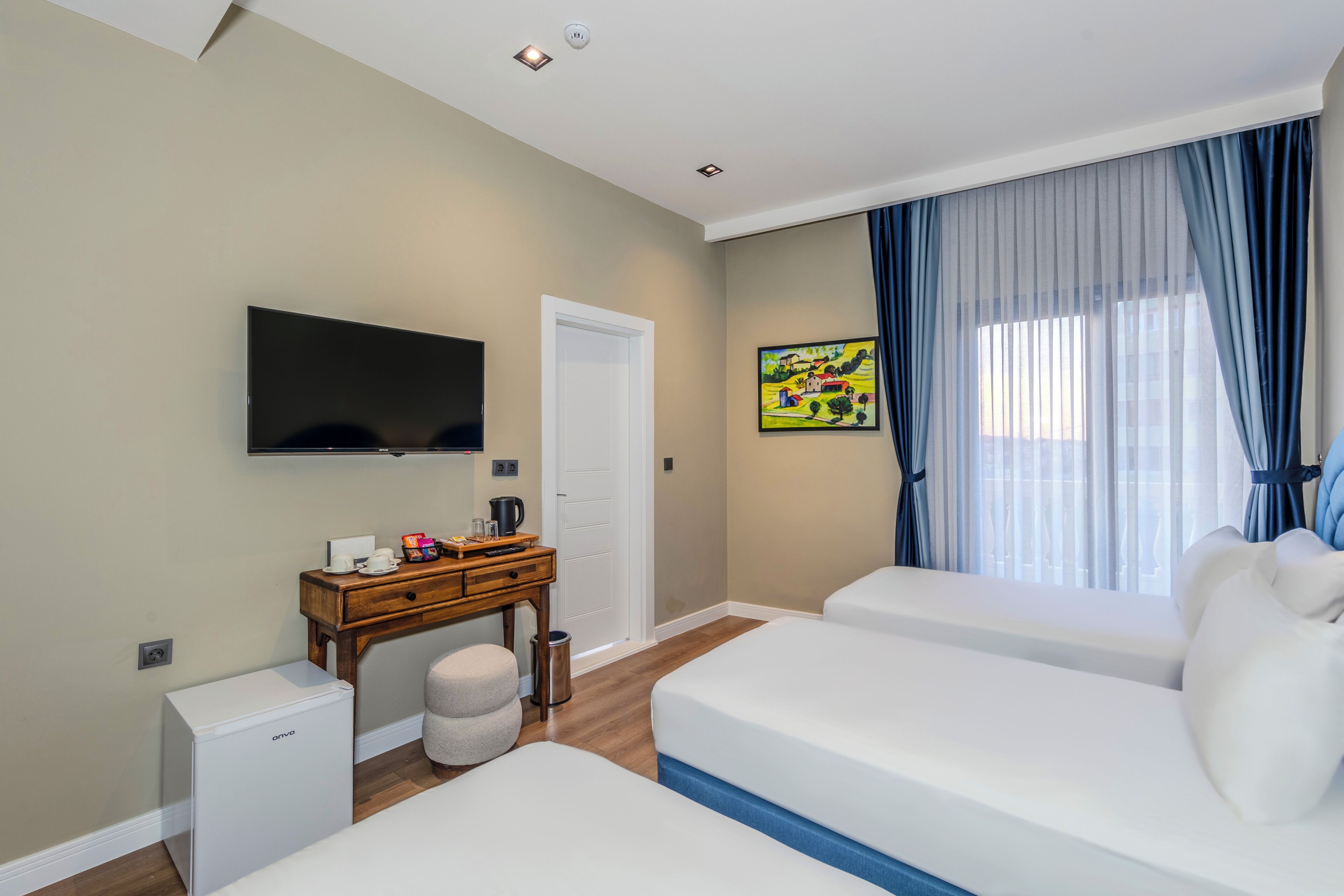 A hotel room with two beds, a TV, a small desk with a coffee maker, and a painting on the wall.