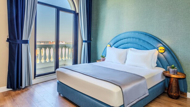 A hotel room with a large bed, a view through a glass door, and a small table with a plant. - Nenesa Hotel İstanbul Airport  (Arnavutkoy)