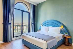 Habitación de hotel con una cama grande, vistas a través de un ventanal y una mesita con una planta.