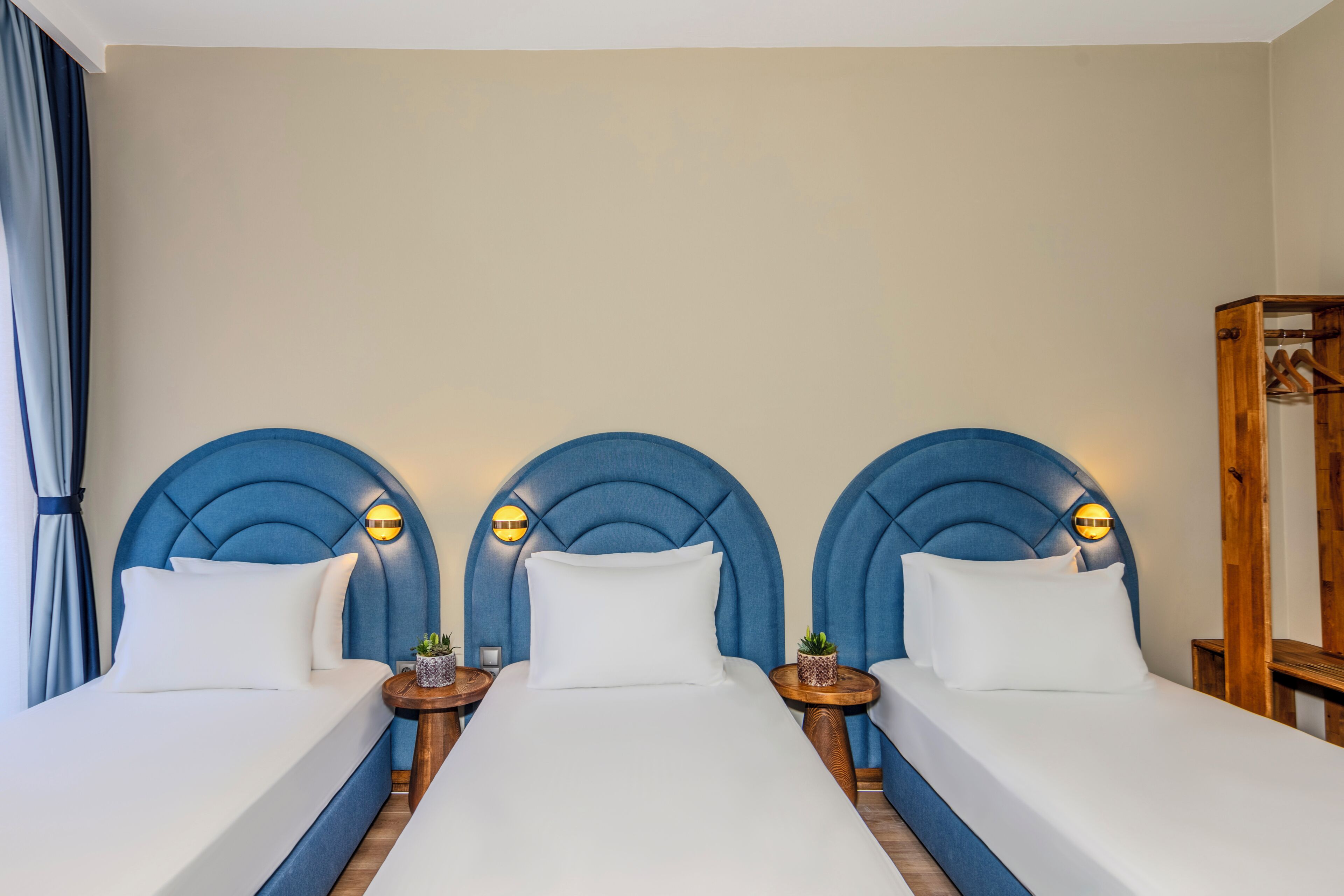 Une chambre d’hôtel avec trois lits, chacun doté d’une tête de lit bleue et d’une petite table de chevet avec une lampe.