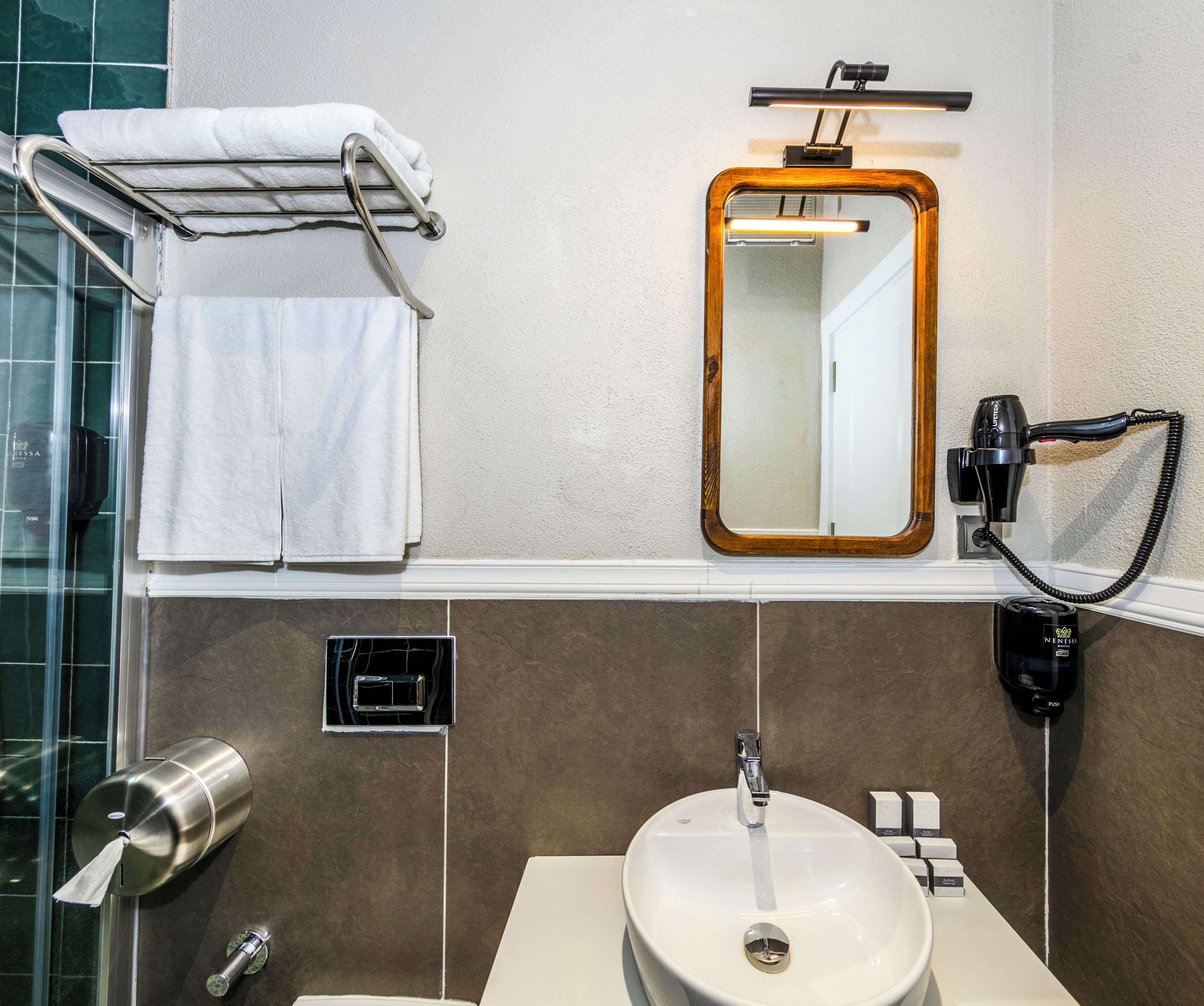 A bathroom with a sink, mirror, towel rack, hairdryer, and a soap dispenser.