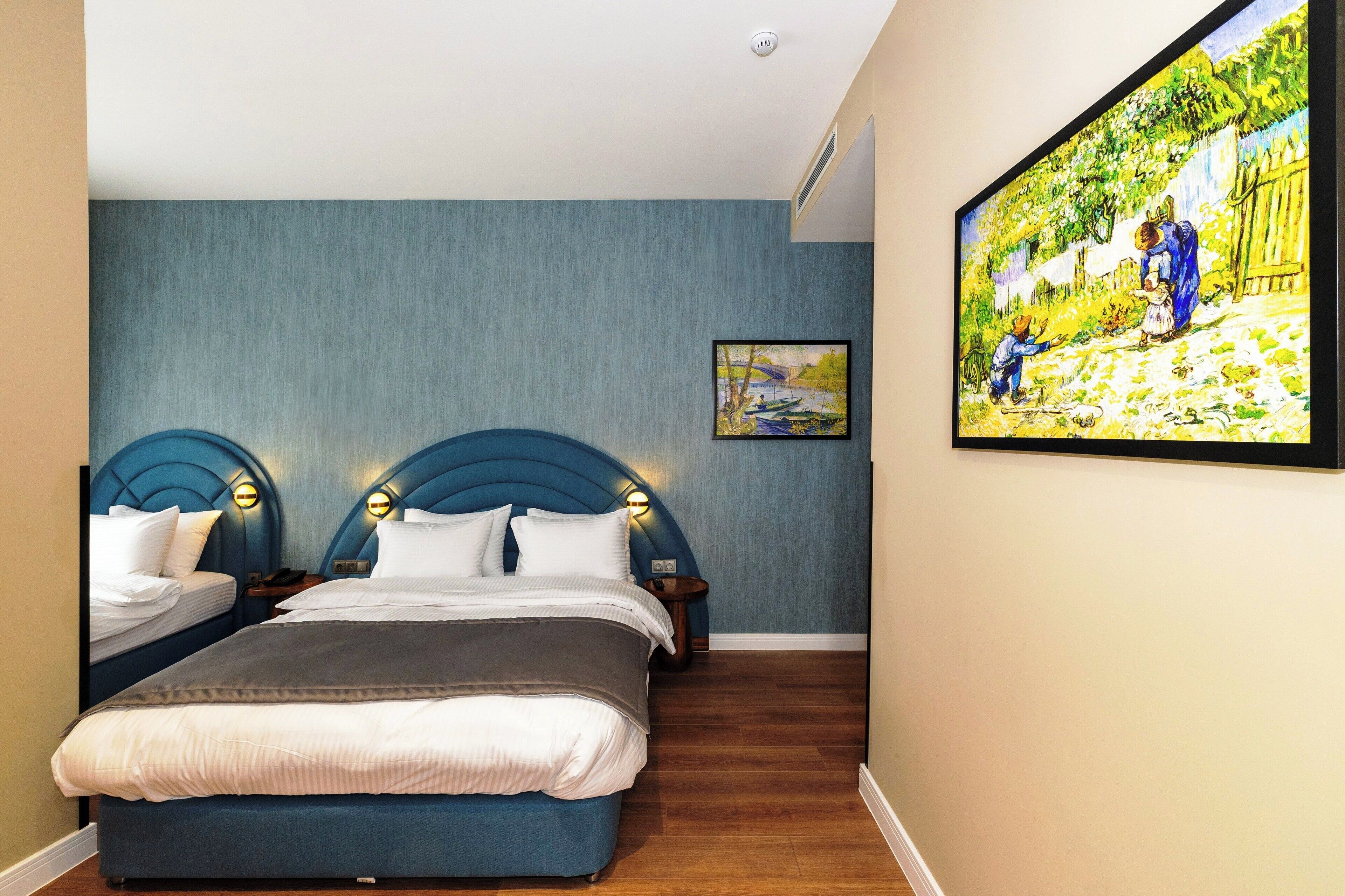 A bedroom with two beds, a large painting on the wall, and a wooden floor.