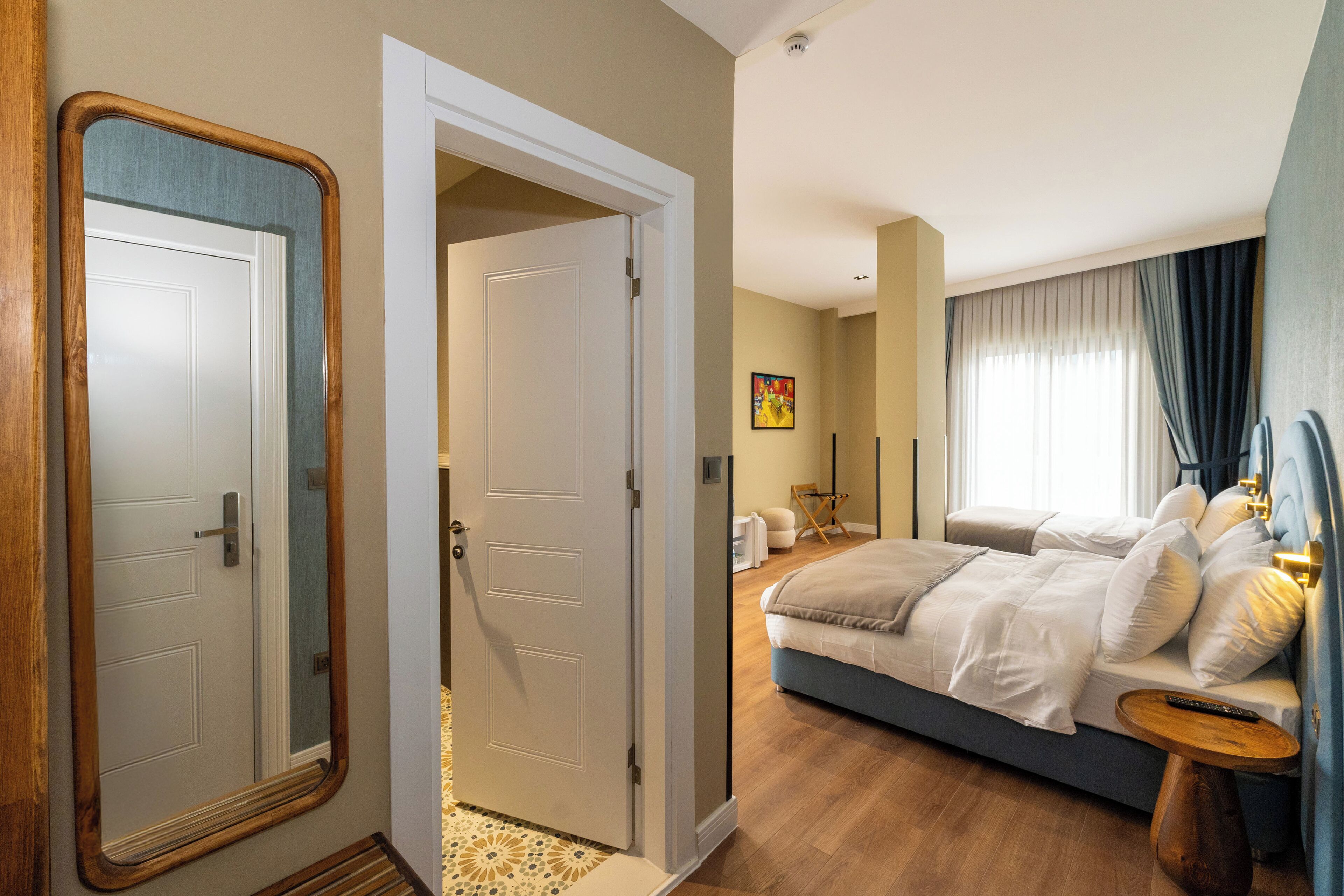 Une chambre d’hôtel avec un grand lit, une table de chevet, un miroir et une porte donnant sur une autre pièce.