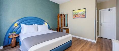 A bedroom with a large bed, a headboard, a bedside table with a lamp, a mirror, and a door.