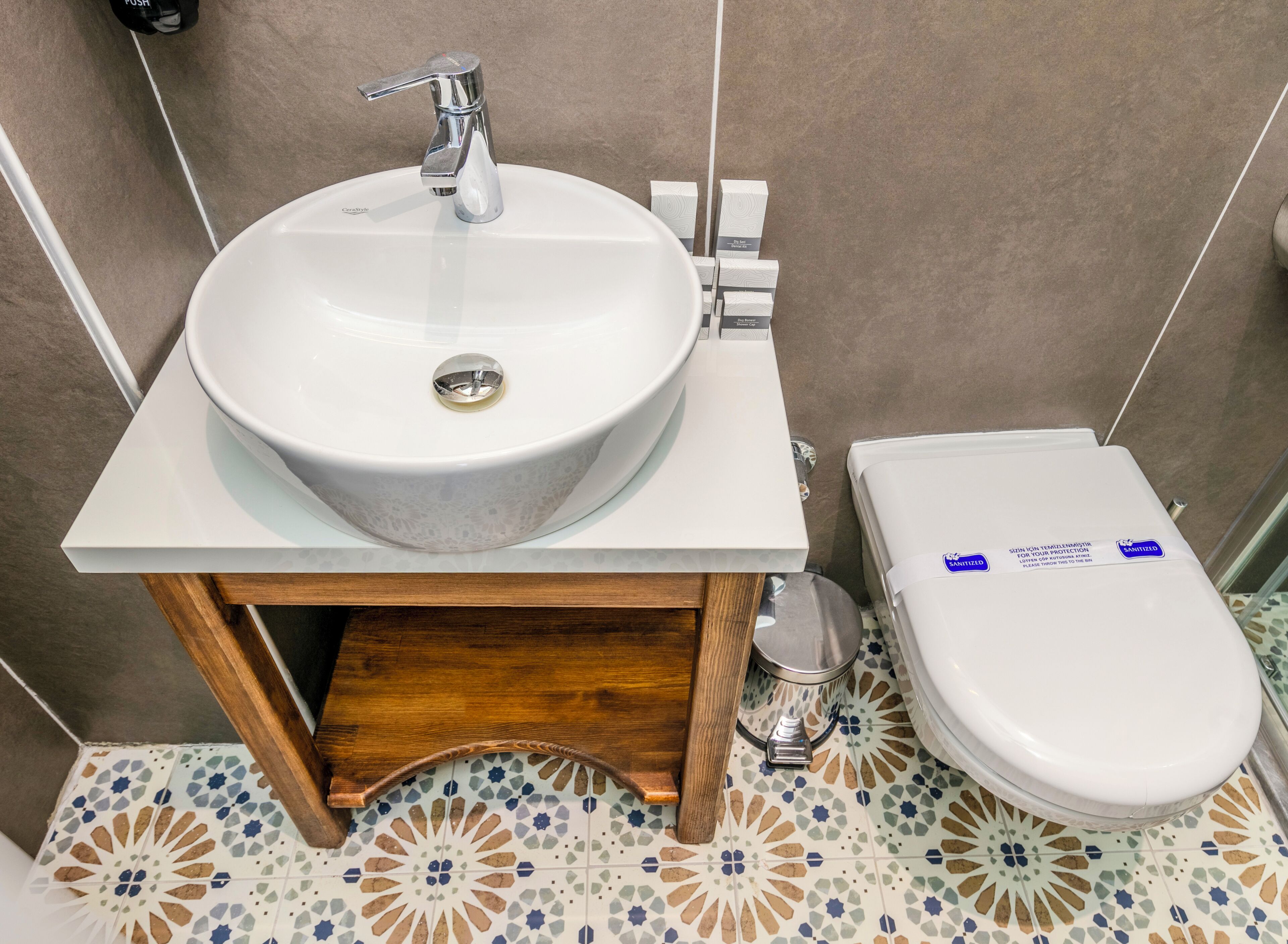 A bathroom with a white sink, a wooden vanity, a toilet, and patterned floor tiles.