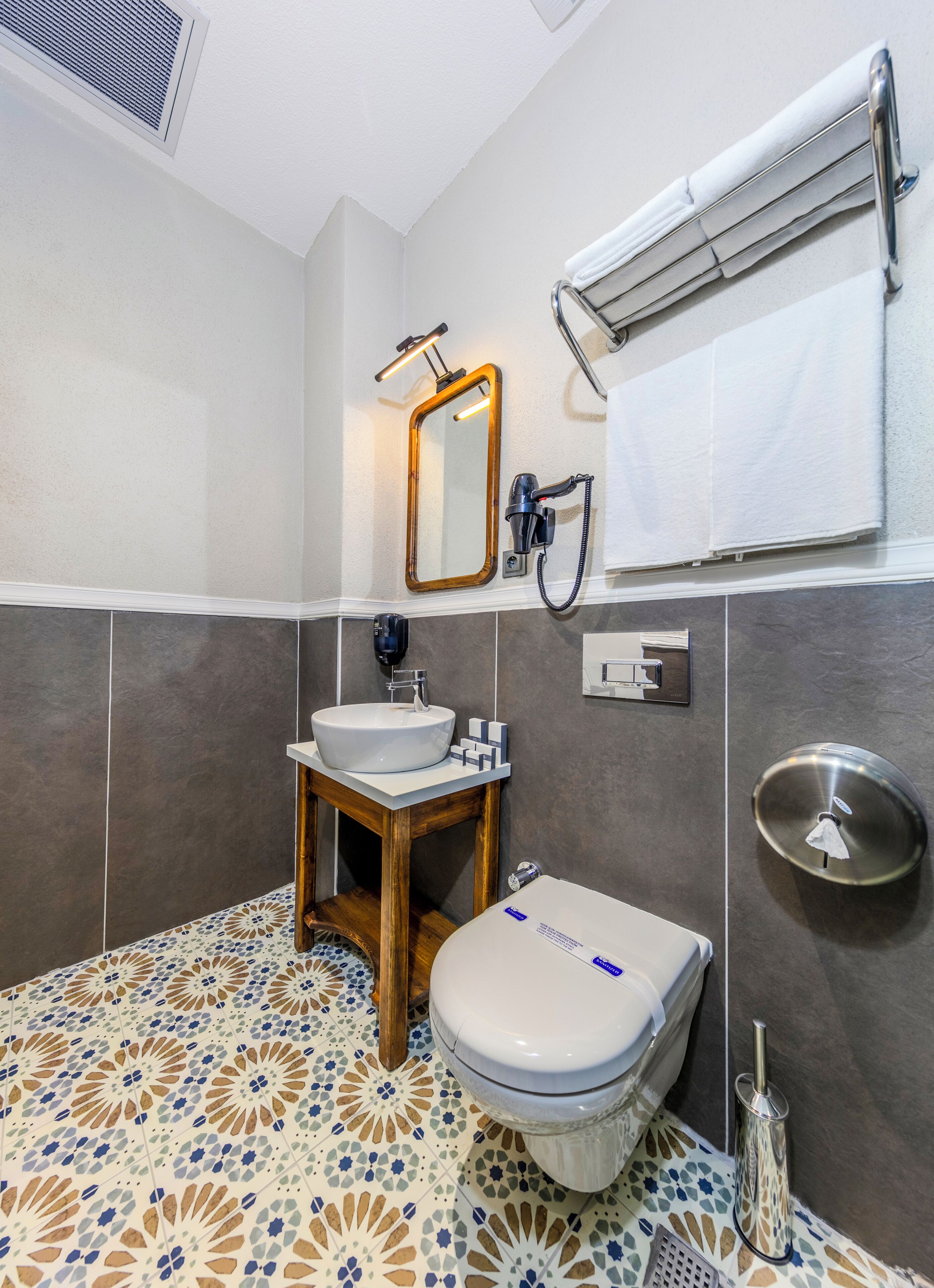 A bathroom with a white sink, wooden vanity, a toilet, a mirror, and a towel rack.