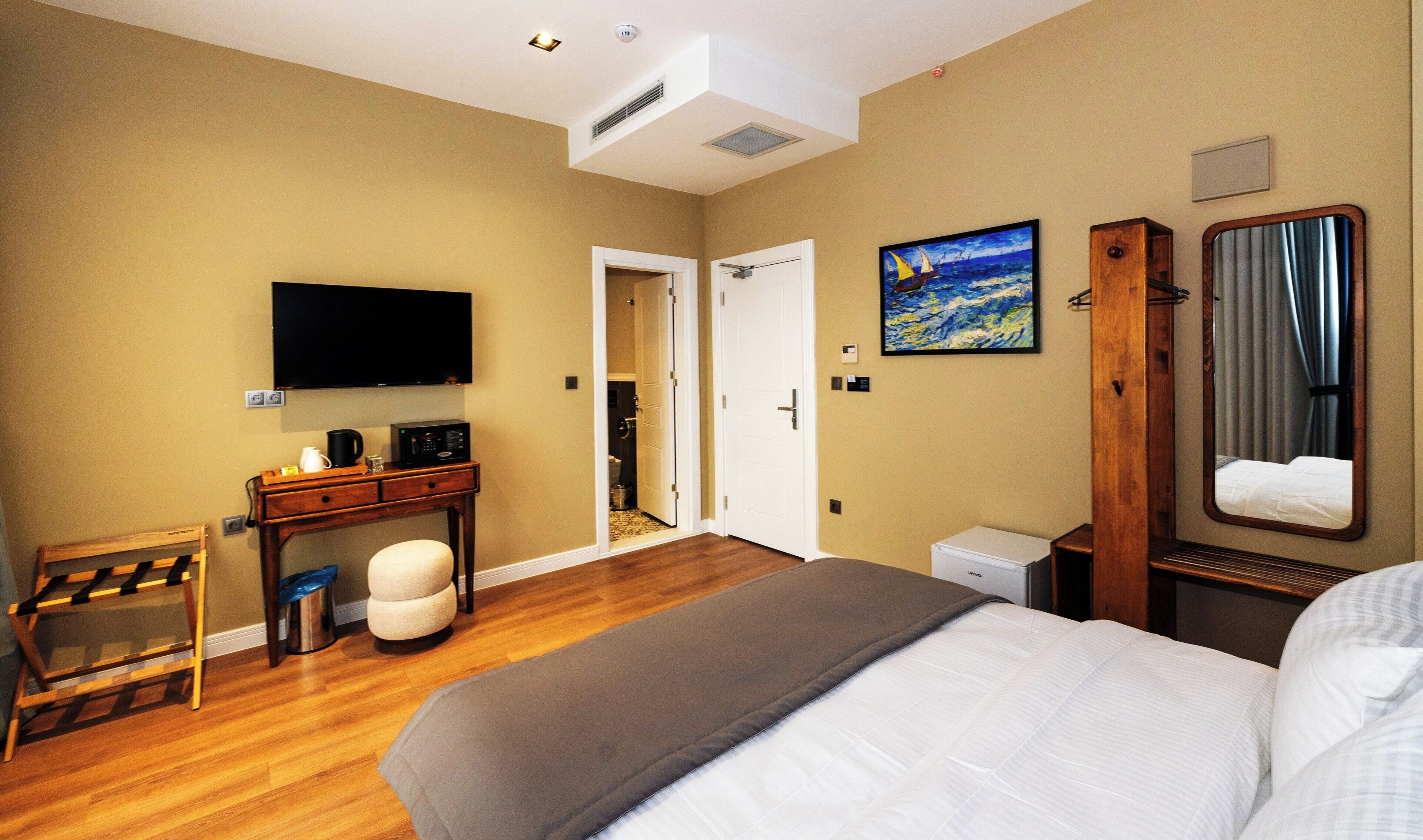 A hotel room with a bed, a desk with a computer, a TV, and a painting on the wall.
