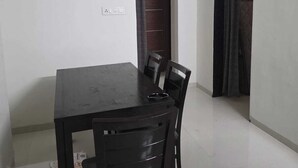 A dining area with a table and four chairs, a ceiling fan, and a door leading to another room. - Wellnessghar (Panvel)
