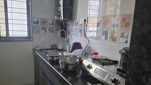 A compact kitchen with a gas stove, a sink, and a window with a view. - Wellnessghar (Panvel)