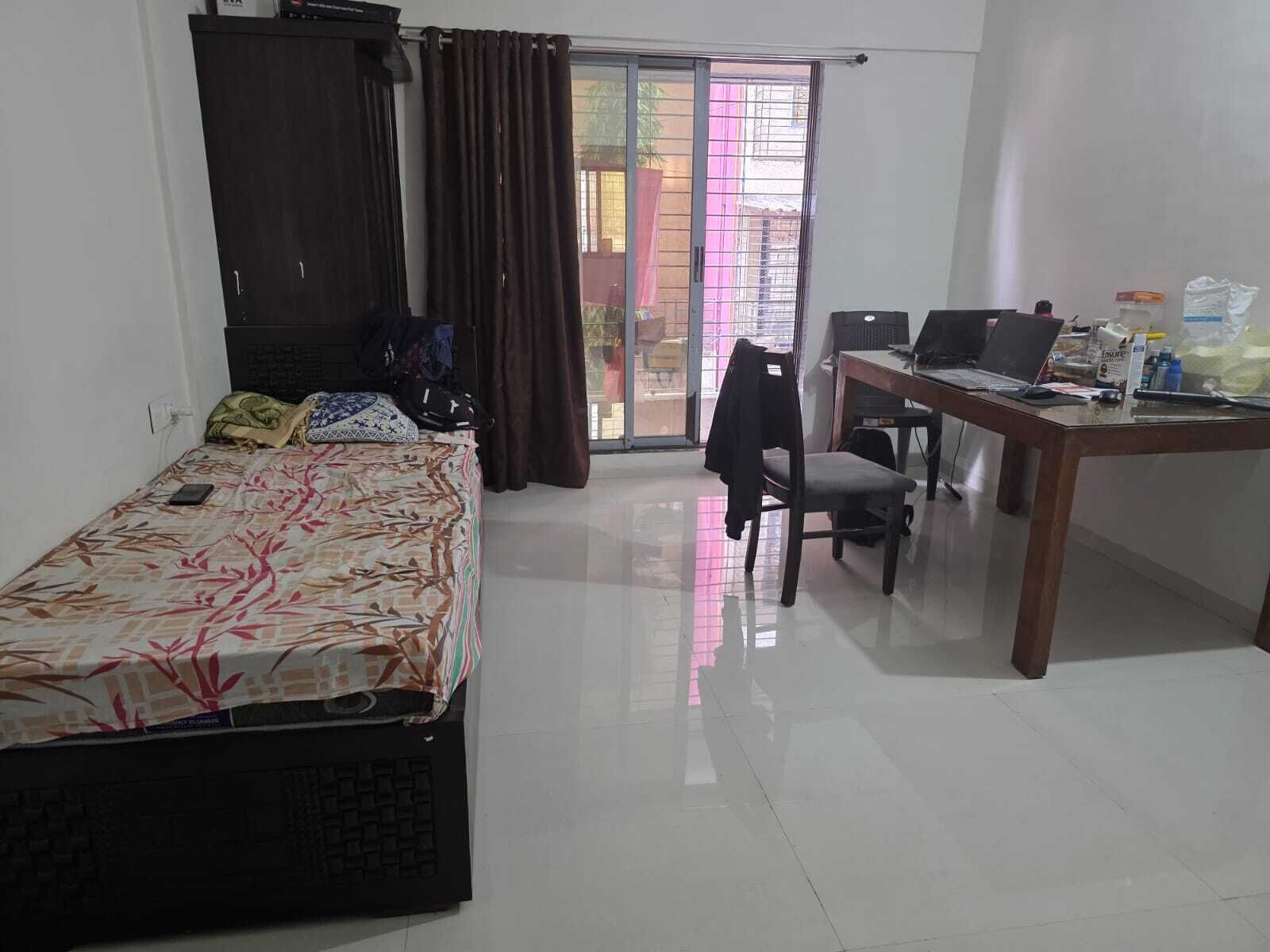 A bedroom with a bed, a desk, and a chair. There is a window with curtains and a view of the outside.