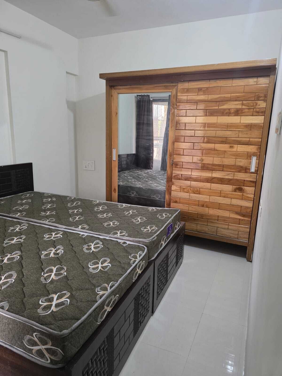 A bedroom with a bed, a wooden wardrobe, and a sliding door leading to a balcony.
