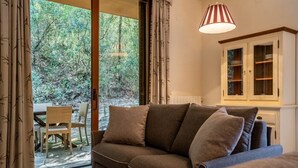 Ein gemütliches Wohnzimmer mit einer Couch, einem Esstisch mit Stühlen und Blick auf einen Wald durch ein großes Fenster.