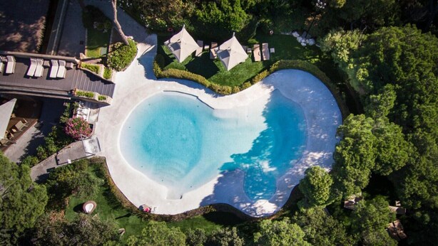 Eine Luftaufnahme von einem Resort mit einem großen, runden Swimmingpool, umgeben von üppiger Vegetation und einigen Liegestühlen.