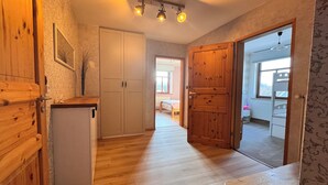 Un couloir au sol en bois, un réfrigérateur blanc et une porte en bois donnant sur une chambre.