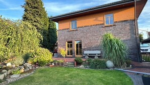 Une maison à deux étages avec une façade en briques, une pelouse bien entretenue et une variété de plantes et d’arbres.