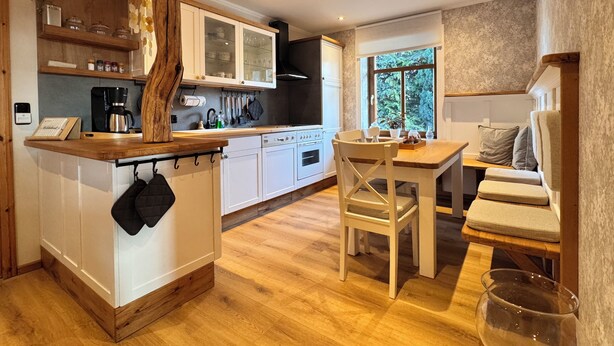 Une cuisine moderne avec des meubles blancs, un îlot central en bois et un coin repas comprenant une table et des chaises.