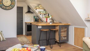 A modern kitchen with a central island, bar stools, and a dining area with a sofa. - Peaceful Stylish Entire Apartment - Views, Gardens, Firepit, Balcony (Holt)
