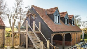 A wooden cabin with a steep roof, a wooden staircase, and a small porch. - Peaceful Stylish Entire Apartment - Views, Gardens, Firepit, Balcony (Holt)