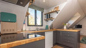 A modern kitchen with a central island, built-in appliances, and a window providing natural light. - Peaceful Stylish Entire Apartment - Views, Gardens, Firepit, Balcony (Holt)
