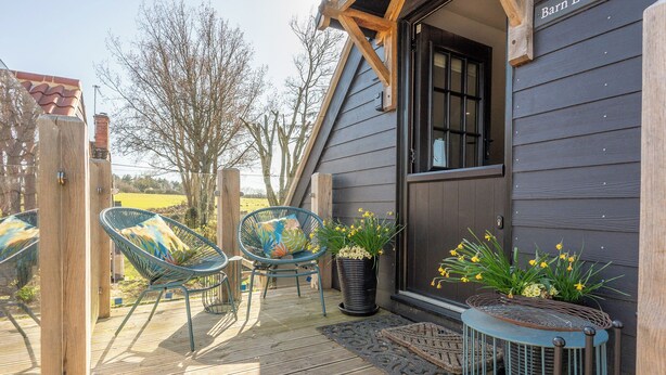 A wooden deck with two chairs and a small table, a potted plant, and a door labeled 'Barn.' - Peaceful Stylish Entire Apartment - Views, Gardens, Firepit, Balcony (Holt)